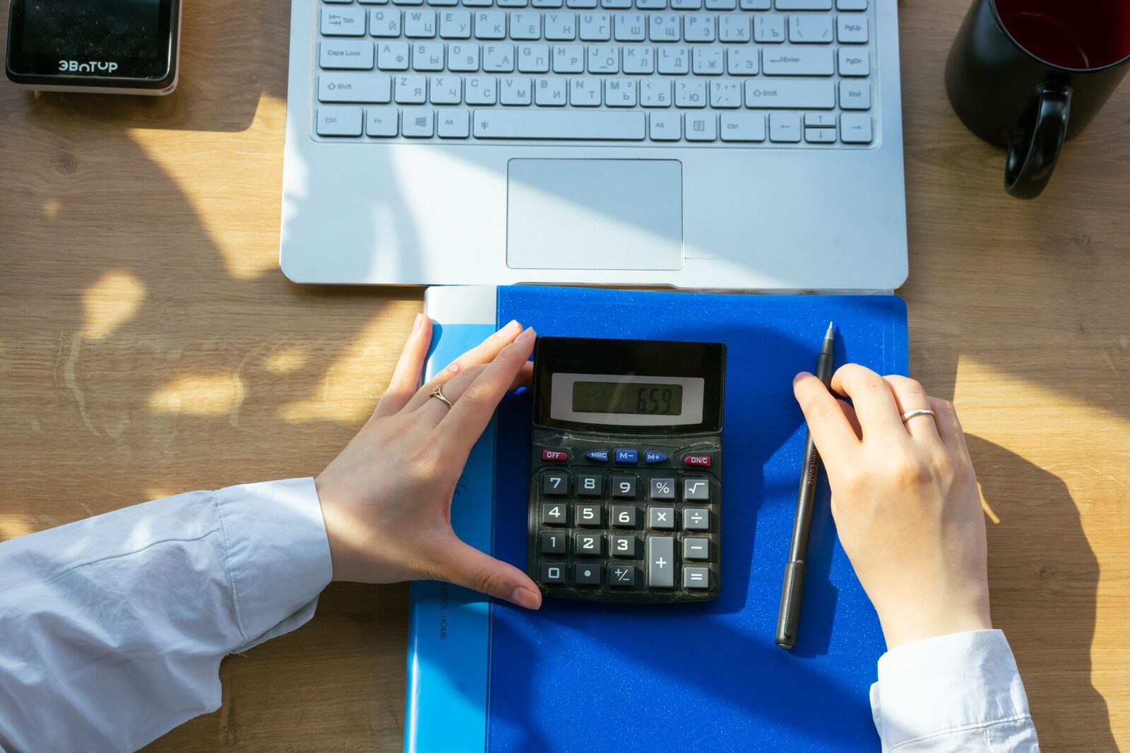 Hands using calculator on a desk with a laptop, pen, and notebook. Perfect for office or finance themes.